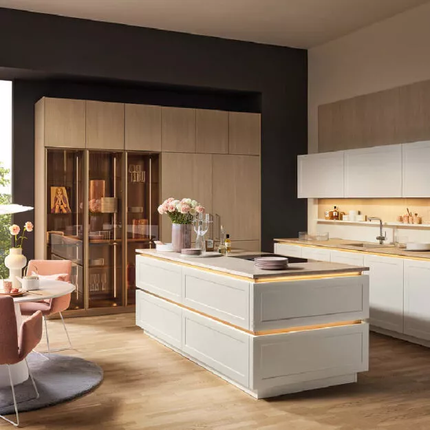 Nolte Landhausküche in Weiß mit Kochinsel, Holz- und Glasvitrinen, integrierten Geräten und warmer Beleuchtung, elegant für gemütliches Kochen
